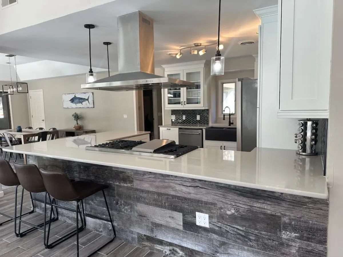 An inviting kitchen scene with a prominent island, stainless steel hood, comfortable bar stools, and a glimpse into the adjacent dining area. The setting captures the open flow from kitchen to dining—ideal for group gatherings and celebrations.