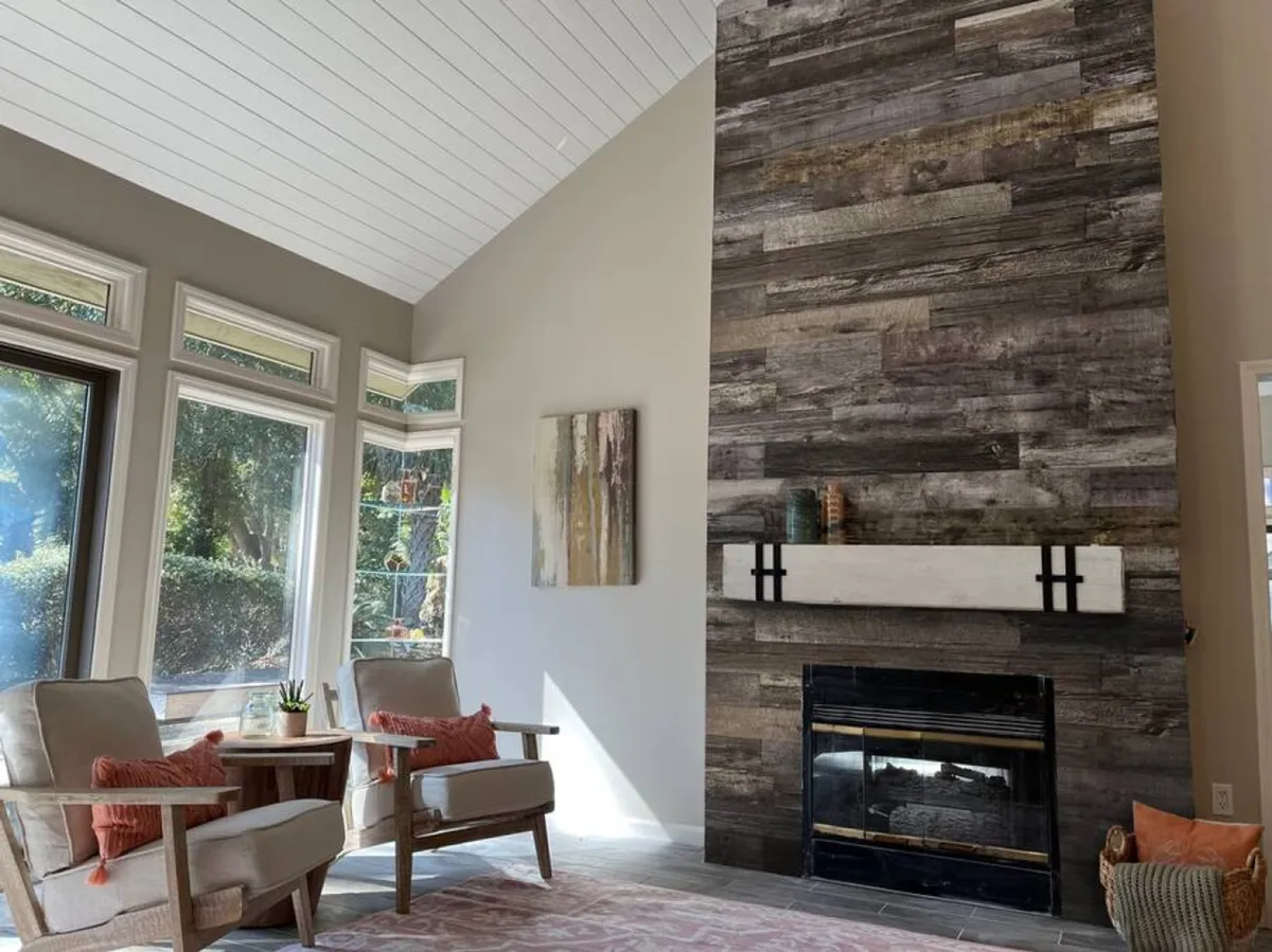 A spacious great room featuring a striking fireplace set into a wooden accent wall, large windows that let in natural light, and a comfortable seating area arranged for both intimate conversations and festive gatherings.
