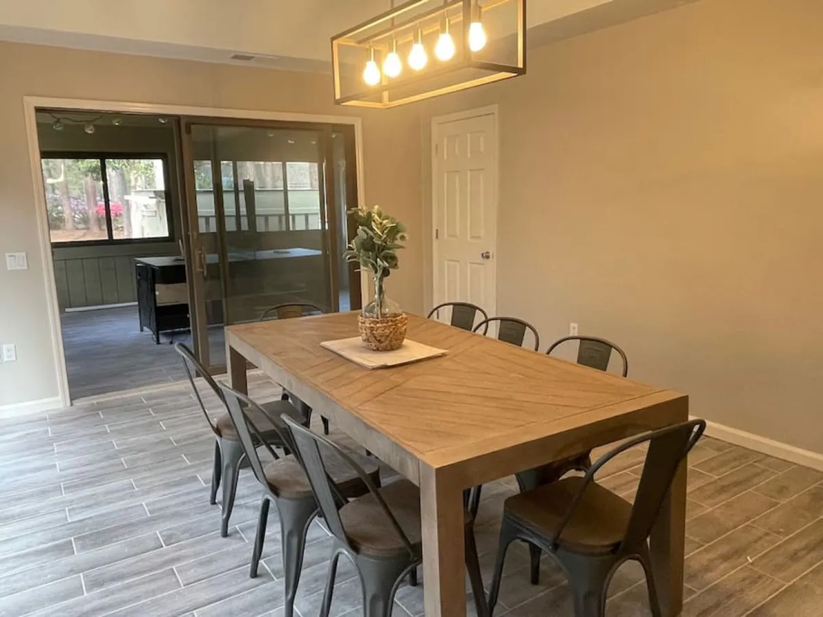 A warm dining space featuring a large wooden table, a stylish overhead light fixture, and a decorative plant centerpiece. The inviting atmosphere sets the scene for family dinners, brunches, and special celebrations.