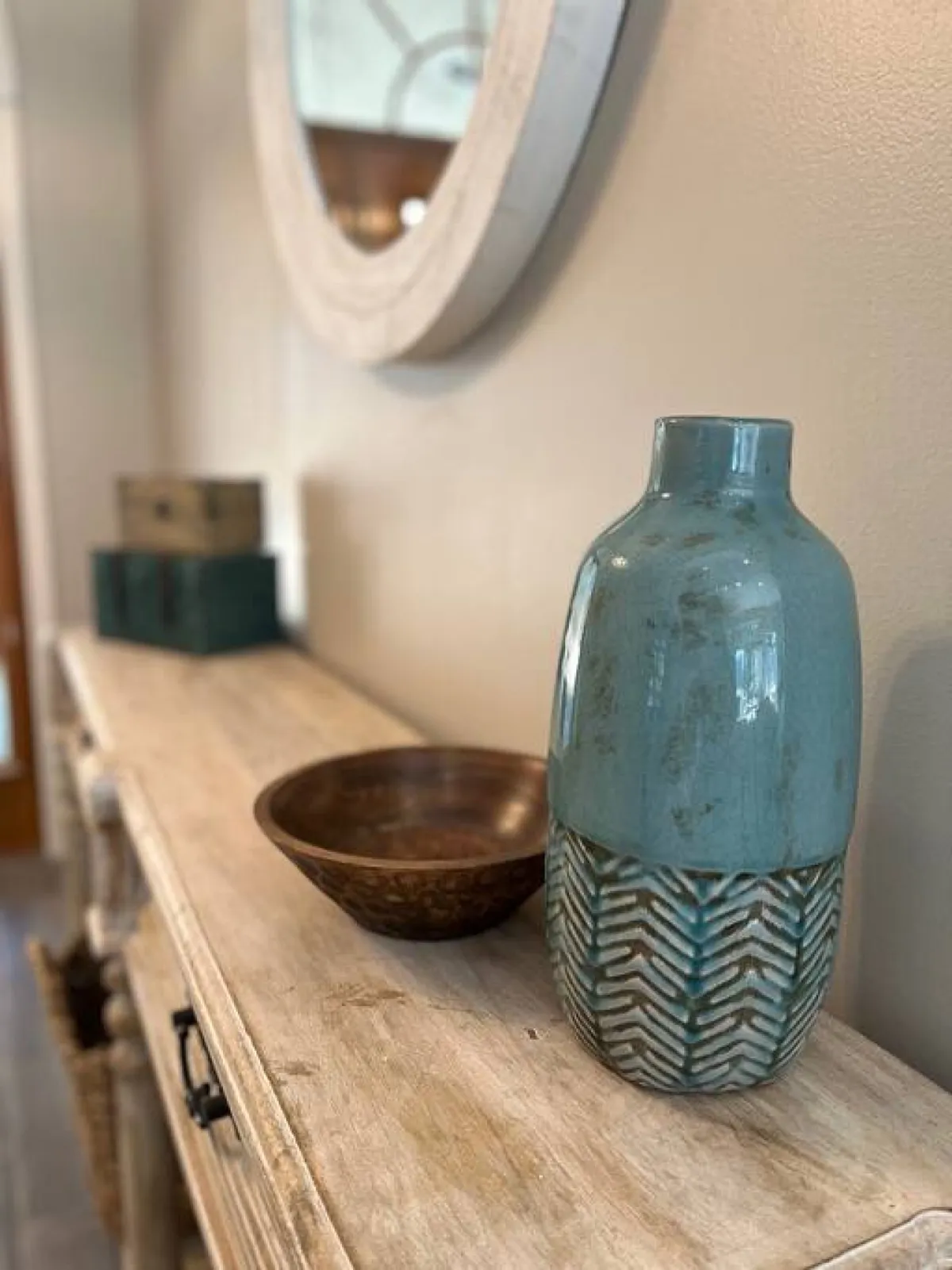 A warmly lit entryway featuring a ceramic vase and a wooden bowl on a console table beneath a mirror. The inviting decor and thoughtful arrangement create a sense of welcome and set the tone for guests entering the home.
