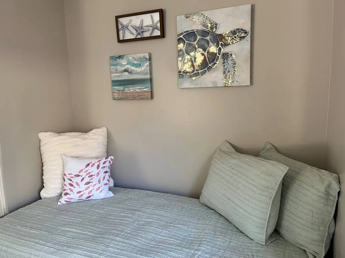 A cozy space accented by coastal-themed decor, including turtle art, seascape paintings, and starfish frames, with decorative pillows inviting quiet relaxation. Natural light enhances the serene, beach-inspired atmosphere.